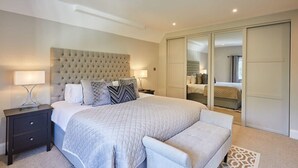 A modern bedroom with a large bed, bedside tables, a bench, and a wardrobe.