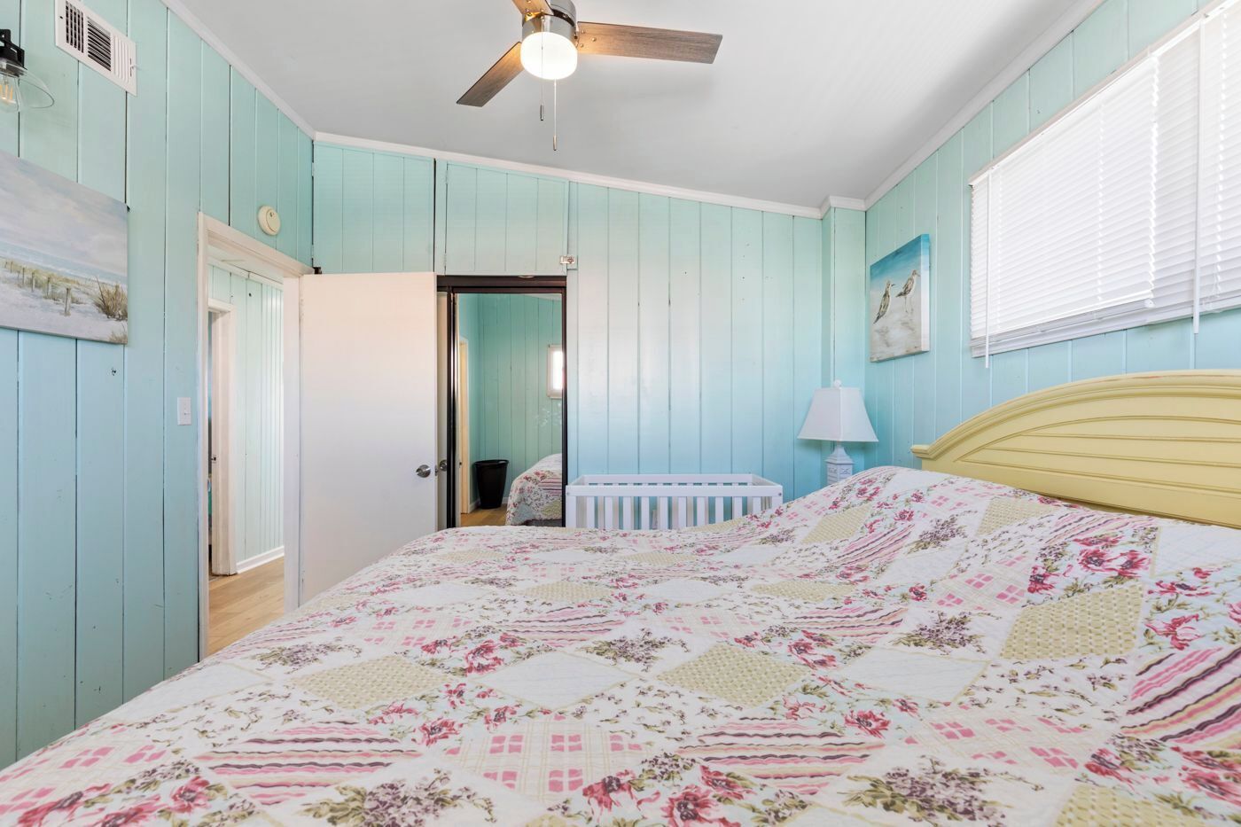 Un dormitorio con una cama, un ventilador de techo, una cuna y una ventana con persianas.