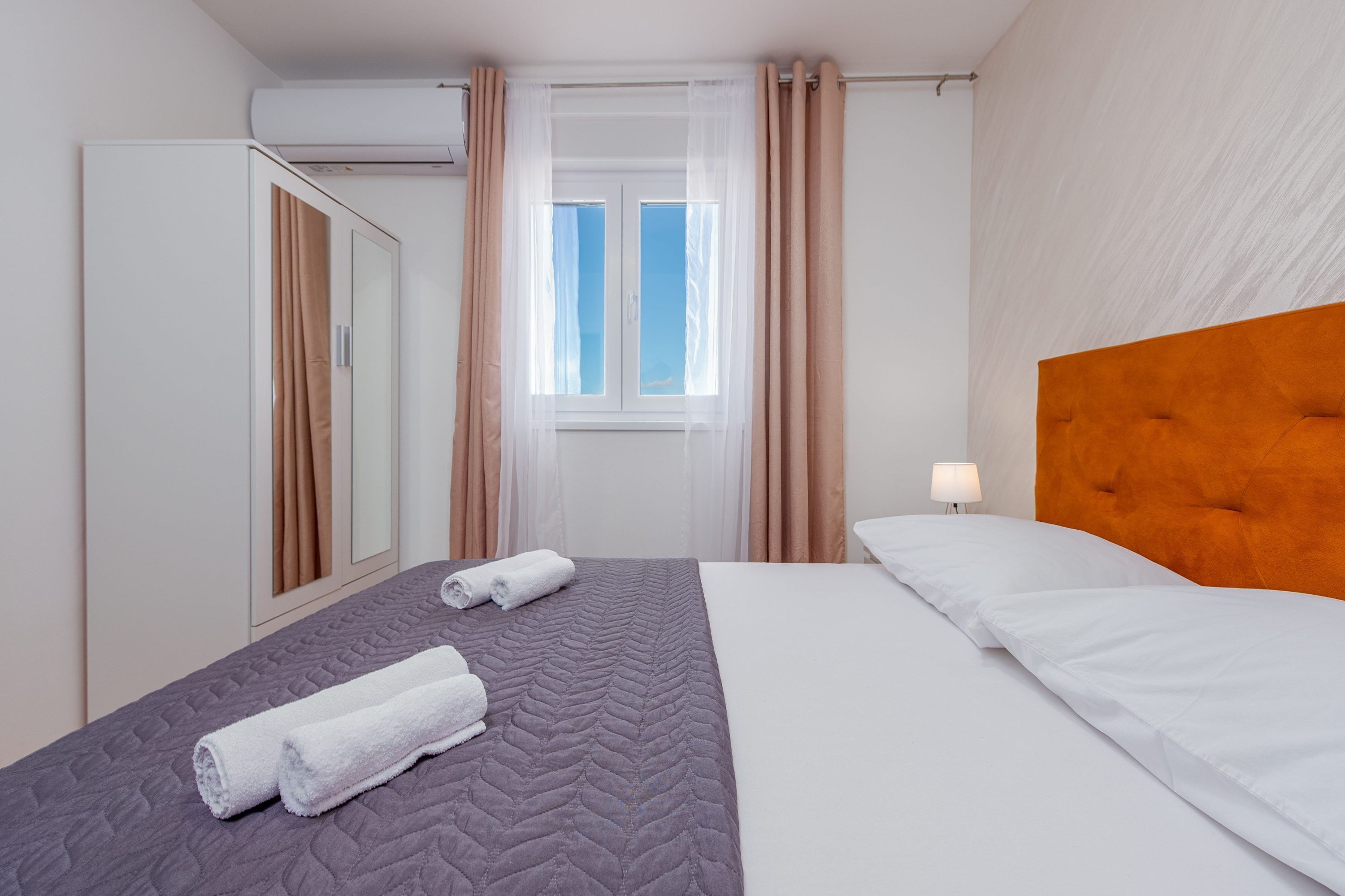 Una camera d'albergo con un letto, un armadio, una finestra con tende e una lampada da comodino.