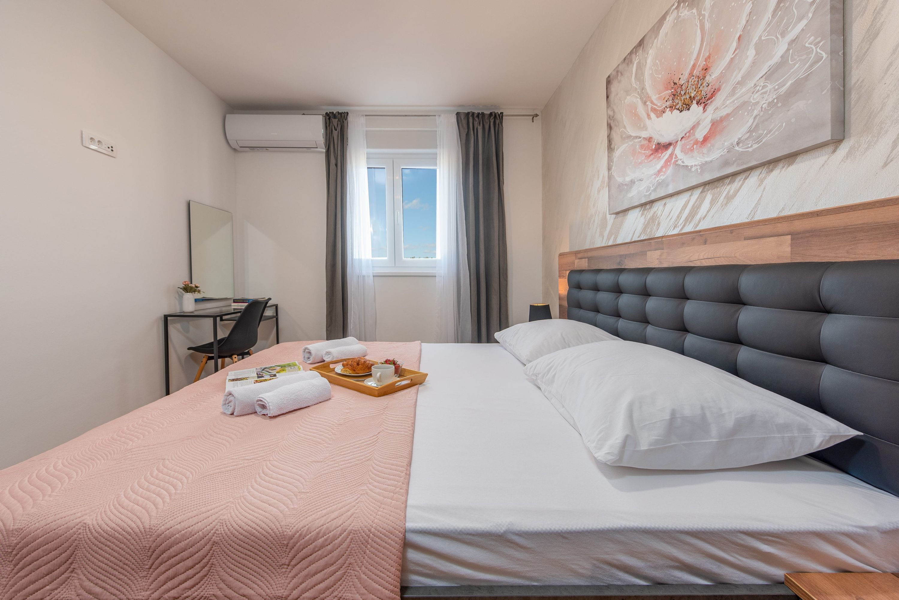 Hotelkamer met een bed, bureau, stoel, raam met gordijnen en een schilderij aan de muur.