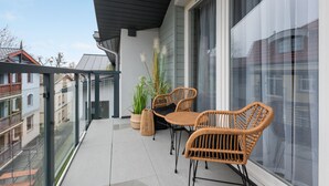 Un balcon avec deux fauteuils en osier, une plante en pot et une vue sur les bâtiments voisins.