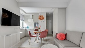 Un salon moderne avec un canapé gris, un coin repas avec une table et des chaises, et une cuisine en arrière-plan.