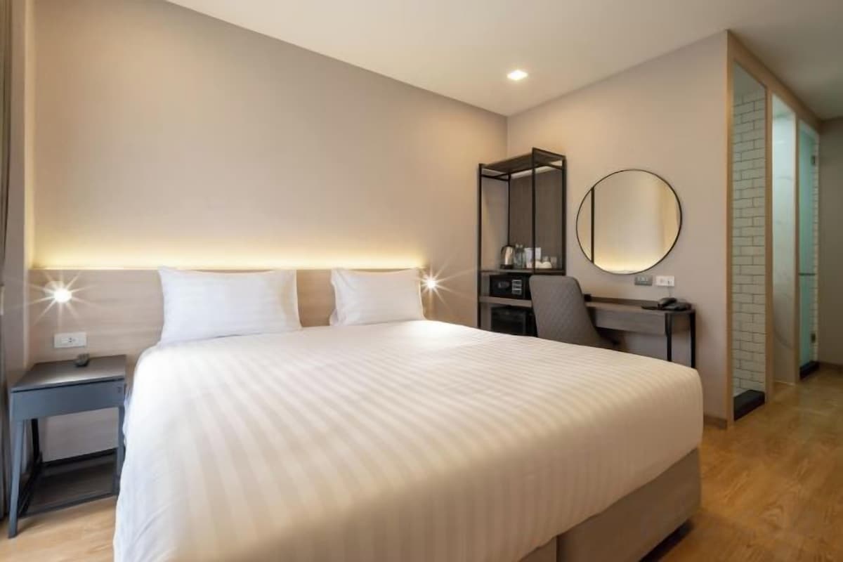 A hotel room with a large bed, bedside tables, a desk with a chair, a mirror, and a wardrobe.