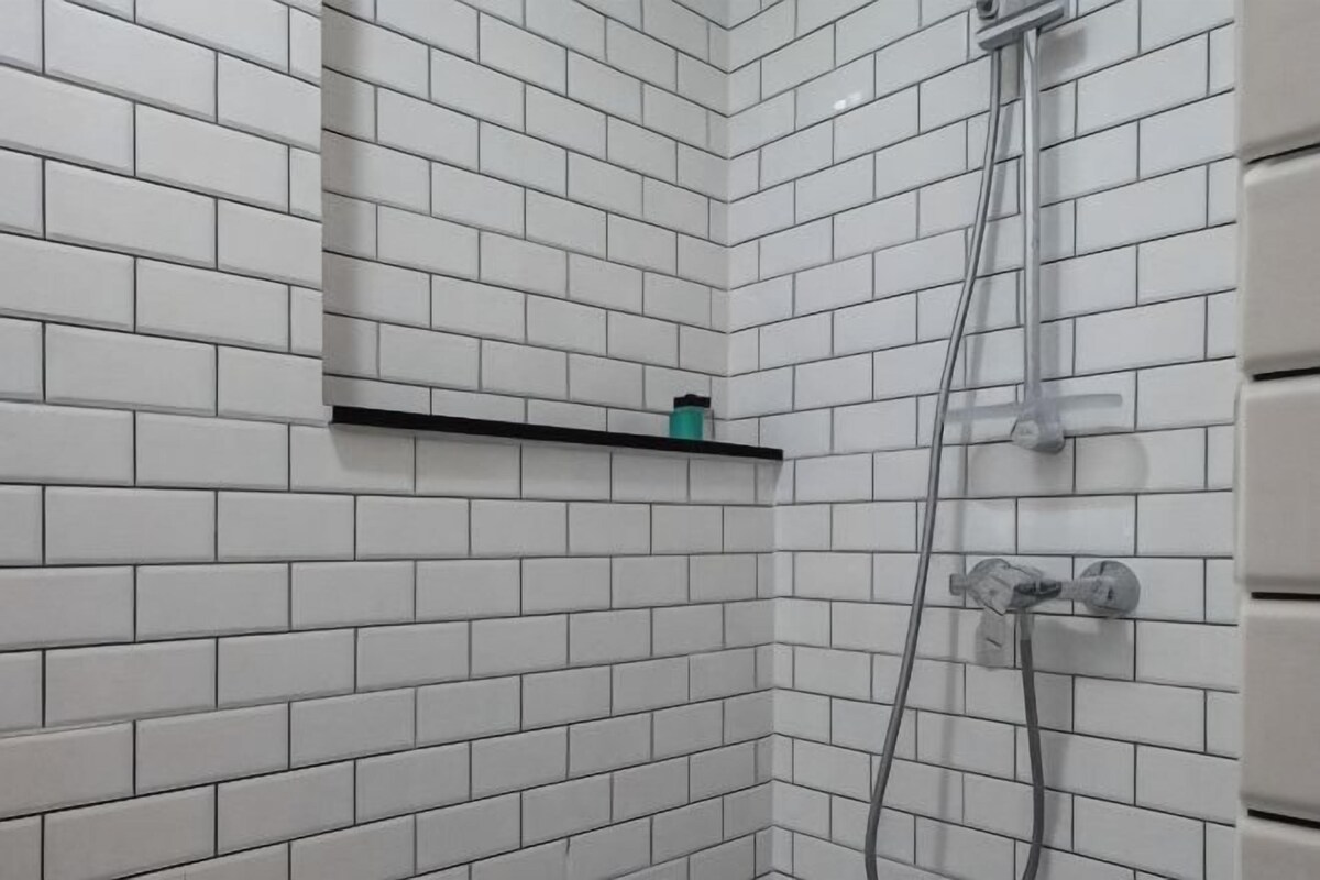 A bathroom with white tiled walls, a black shelf, and a shower area.