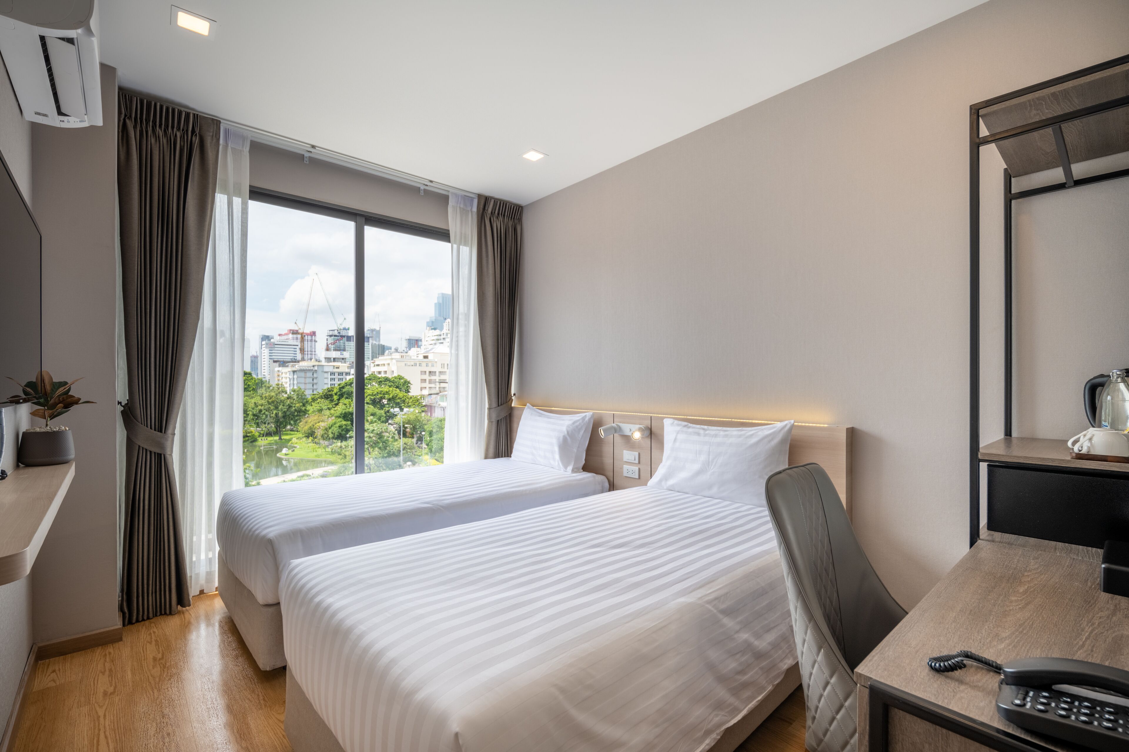 A hotel room with two beds, a desk, a chair, and a view of the city.