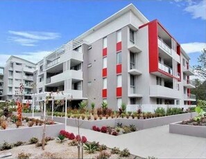 Stylish building with flat roofline, large windows, and balconies overlooking a beautifully maintained garden.