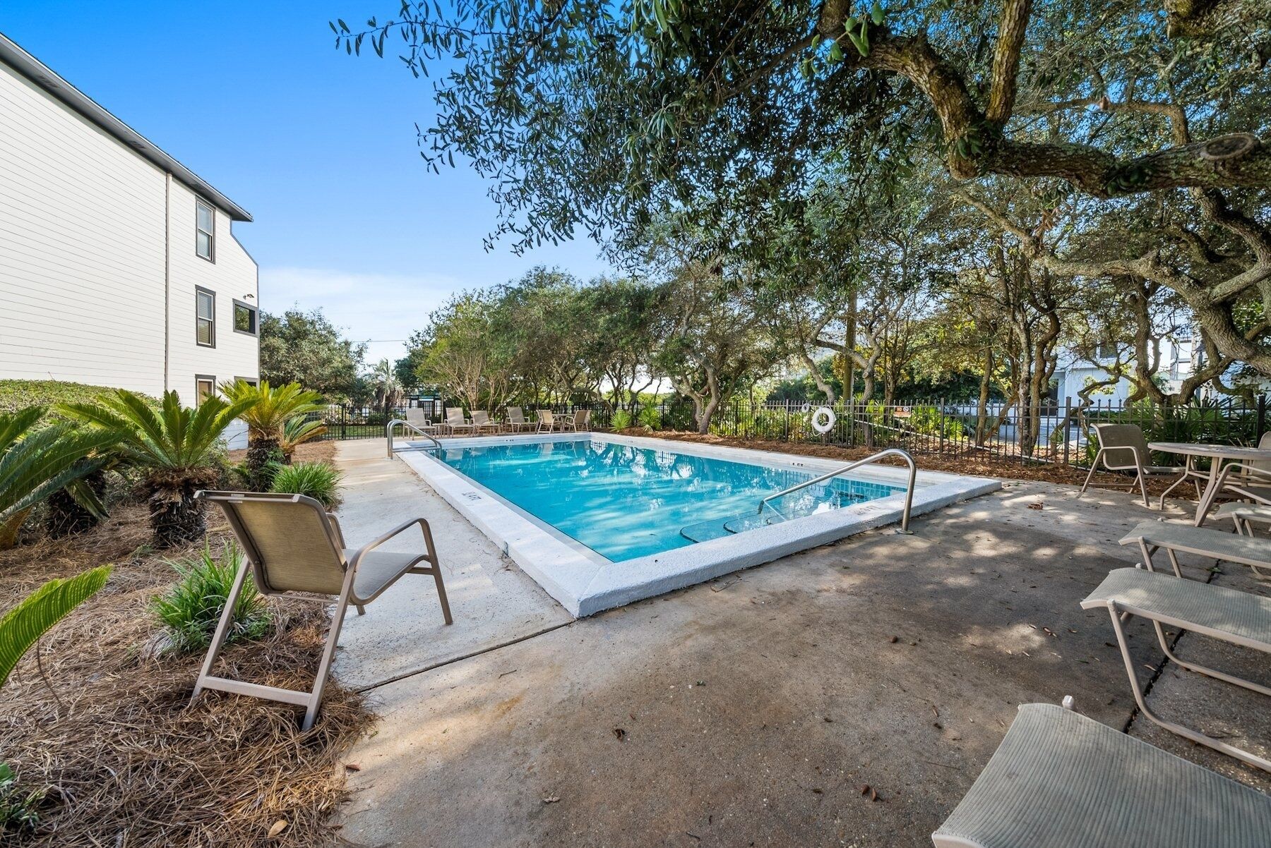 Piscina retangular com borda de concreto, rodeada por espreguiçadeiras e um deck de concreto.