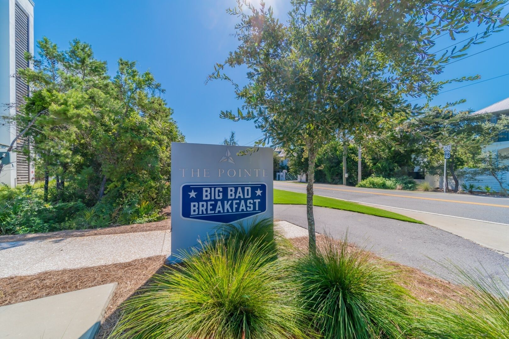 A sign for 'The Point Big Bad Breakfast' with a clear view of the surrounding greenery and a road.