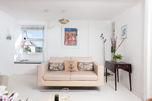 A modern living room with a beige sofa, a small side table, and a window with a view of the outside.
