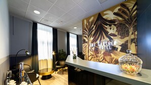 Zona de recepción de hotel con diseño moderno, que incluye un mostrador de recepción, área de descanso y una pared decorativa con el nombre del hotel.