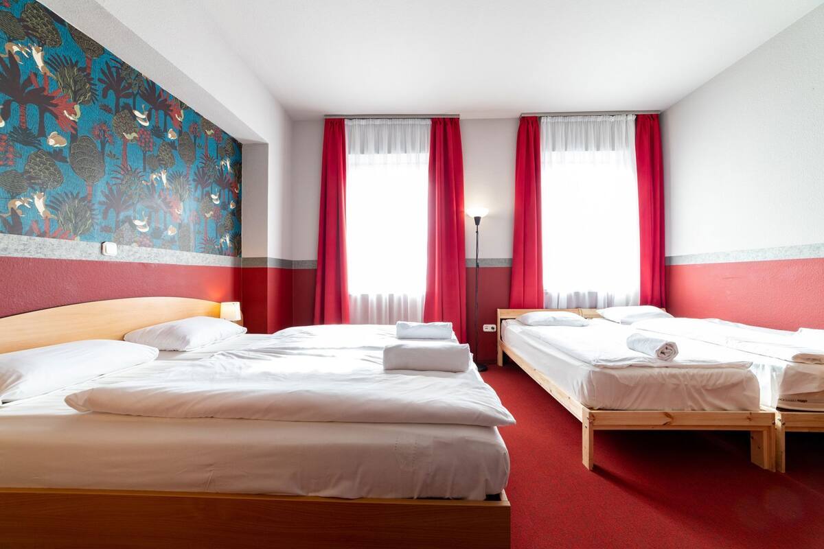 A hotel room with two beds, red curtains, a large abstract painting, and a red carpet.
