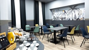 Un comedor moderno con mesas y sillas, productos para el desayuno y un mural de fauna tropical.