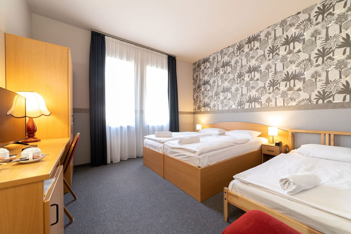 A hotel room with two beds, a desk, a chair, a lamp, and a patterned wall.