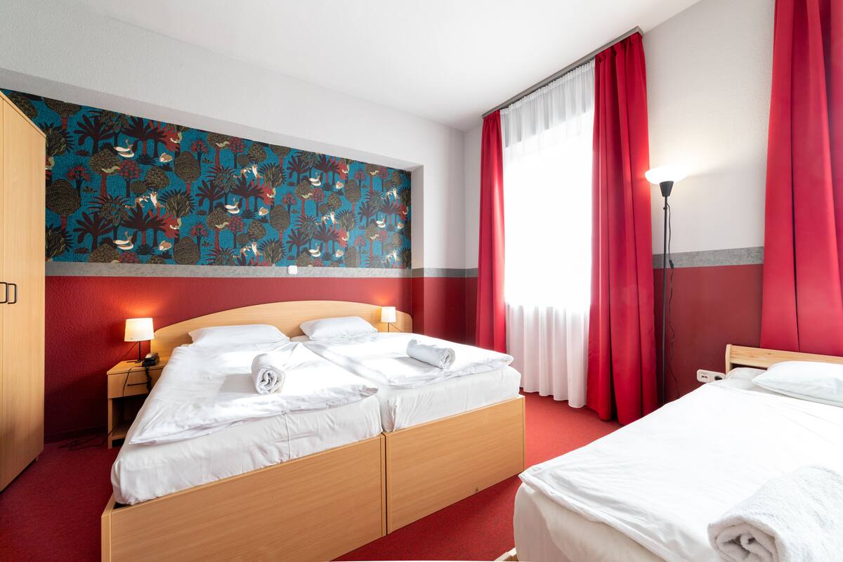 A hotel room with a bed, a nightstand, a lamp, and a red curtain.