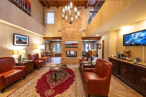 A spacious lobby with leather sofas, a red patterned rug, a fireplace, and a television mounted on the wall.