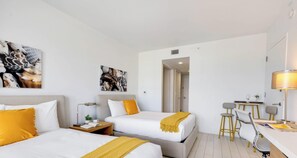 A hotel room with two beds, a desk, a chair, a lamp, and artwork on the walls.