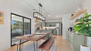 A modern kitchen with a dining area, large windows, and a potted plant.