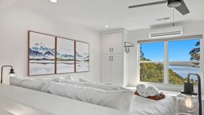 A modern hotel room with a large bed, artwork on the wall, a view of the outdoors, and a ceiling fan.