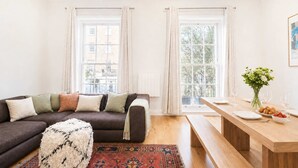 Moderni olohuone, jossa on tummanruskea sohva, kuviollisia koristetyynyjä, valkoinen, pehmeä jalkarah, ja punakuvioinen matto.