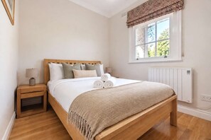Un dormitorio con cama de madera, mesita de noche, ventana con cortina y radiador.