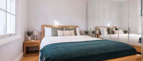 Una camera da letto moderna con un letto in legno, un comodino, uno specchio e una finestra con tende.