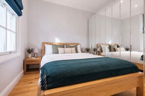 Un dormitorio moderno con una cama de madera, una mesita de noche, un espejo y una ventana con cortinas.