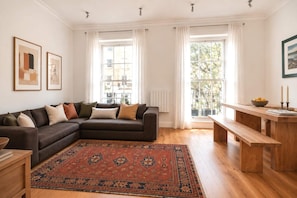 Un salon avec un canapé d’angle marron foncé, un tapis à motifs, un banc en bois et une table à manger décorée de bougies.