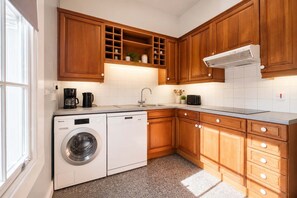Cocina compacta con armarios de madera, horno integrado, lavadora y cafetera.
