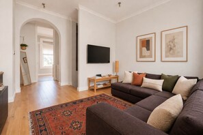 Una sala de estar con un sofá oscuro, un televisor de pantalla plana y una mesa de centro de madera.