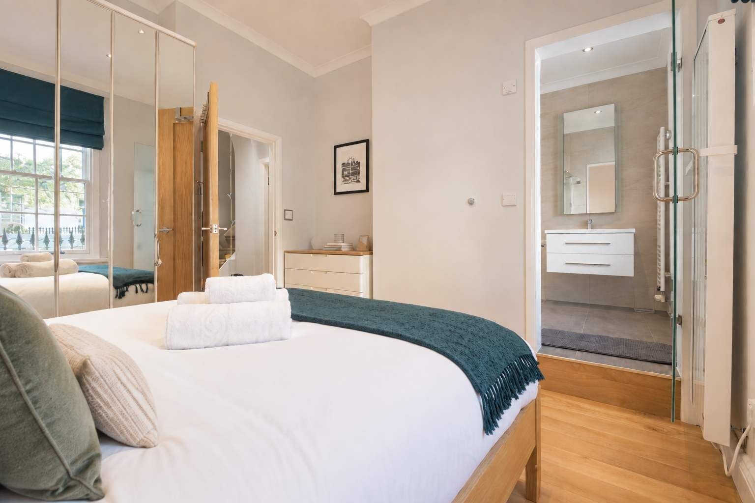 Un dormitorio moderno con una cama grande, una mesita de noche, un armario y un baño visible a través de una puerta abierta.
