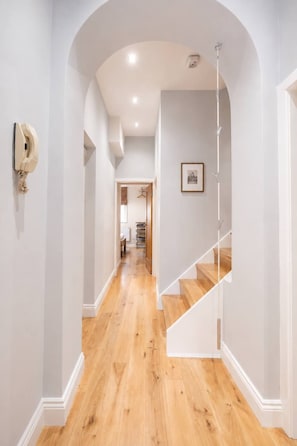Un pasillo con piso de madera, paredes blancas y una escalera con barandillas blancas.