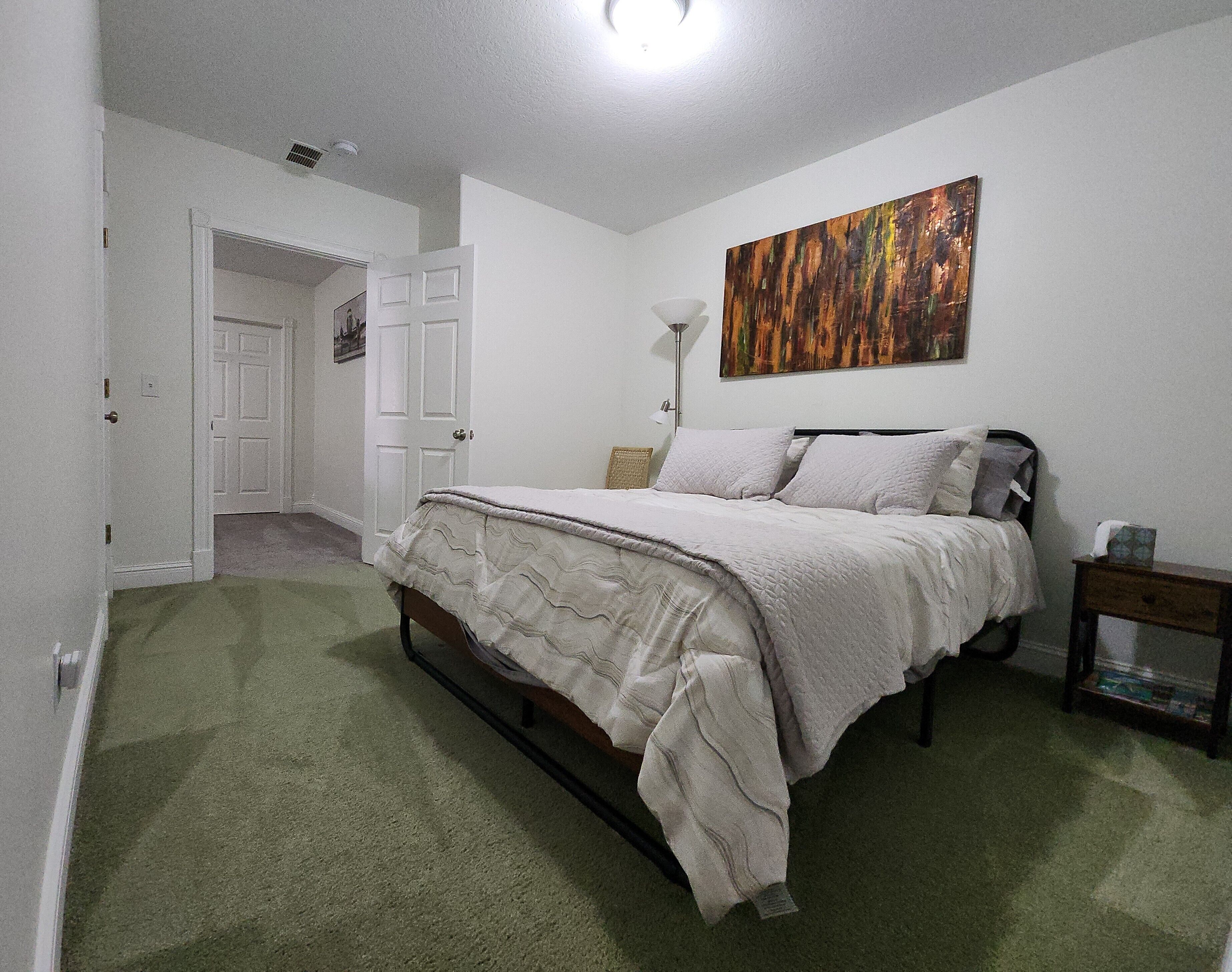 Un dormitorio con una cama, un cuadro, una lámpara y una mesita de noche.