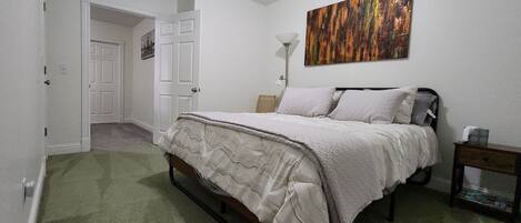 Un dormitorio con una cama, un cuadro, una lámpara y una mesita de noche.