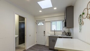 A compact kitchen with a white countertop, a window with blinds, a built-in oven, and a door leading to a bathroom. - @ Marbella Lane - Adorable and Quiet Studio (San Mateo)
