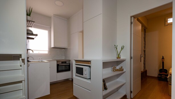 A compact kitchen with white cabinetry, a microwave, and a small shelf with decorative items. - Coqueto Apartamento a 5 Minutos del Retiro (Madrid)