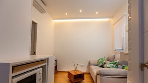 A compact living space with a kitchenette, a wooden side table, and a sofa with decorative pillows. - Coqueto Apartamento a 5 Minutos del Retiro (Madrid)