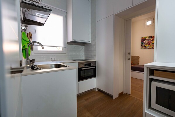 A compact kitchen with white cabinetry, a built-in oven, and a window above the sink. - Coqueto Apartamento a 5 Minutos del Retiro (Madrid)