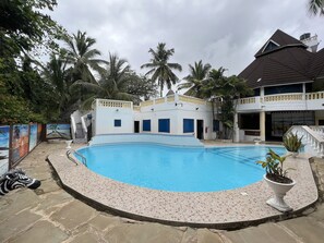 A swimming pool with a tiled deck, surrounded by a building with multiple windows and a balcony.