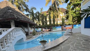 A pool area with a stone floor, a white staircase with balustrades, and a thatched-roof structure. - Charming and Remarkable15-bed Villa in Diani Beach (Diani Beach)