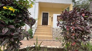 A building with a yellow door, a staircase leading to the entrance, and a white wall with a decorative border. - Charming and Remarkable15-bed Villa in Diani Beach (Diani Beach)