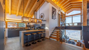 Een moderne keuken met een centraal eiland, barkrukken en een uitzicht op de omgeving door grote ramen.