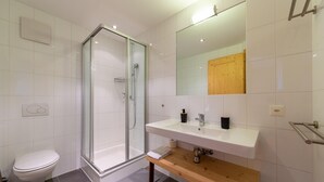 Een moderne badkamer met een glazen douchecabine, een witte wastafel en een houten bankje.