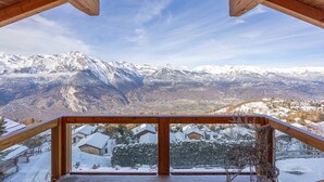 Een houten balkon met uitzicht op besneeuwde bergen en een dorp beneden.