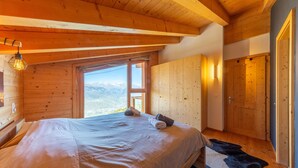 Een slaapkamer in een houten hut met een bed, een raam en een deur.