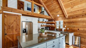 A modern kitchen with wooden beams, white cabinets, and a stainless steel refrigerator.