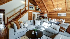 A spacious living area with a large L-shaped sectional sofa, a black coffee table, and a staircase leading to an upper level.