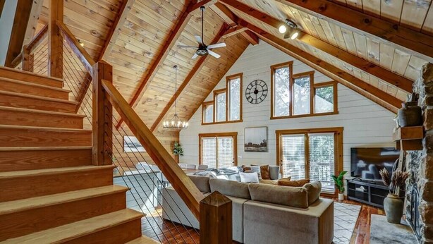 A spacious loft with a wooden staircase, a large sofa, and a stone fireplace.