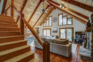 A spacious loft with a wooden staircase, a large sofa, and a stone fireplace.