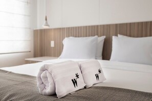 A neatly made bed with white linens and pillows, a patterned throw blanket, and a wooden headboard.