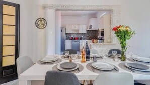 A dining area with a table set for four, a kitchen in the background, and a clock on the wall. - Ardeche in Provence with shady park (Pont-Saint-Esprit)